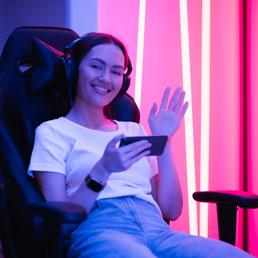 Girl relaxing playing games on mobile phone and sitting on a gaming chair. Room with colorful neon light